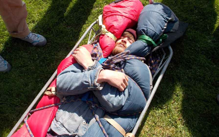 a person lies in a stretcher during a wilderness first responder training